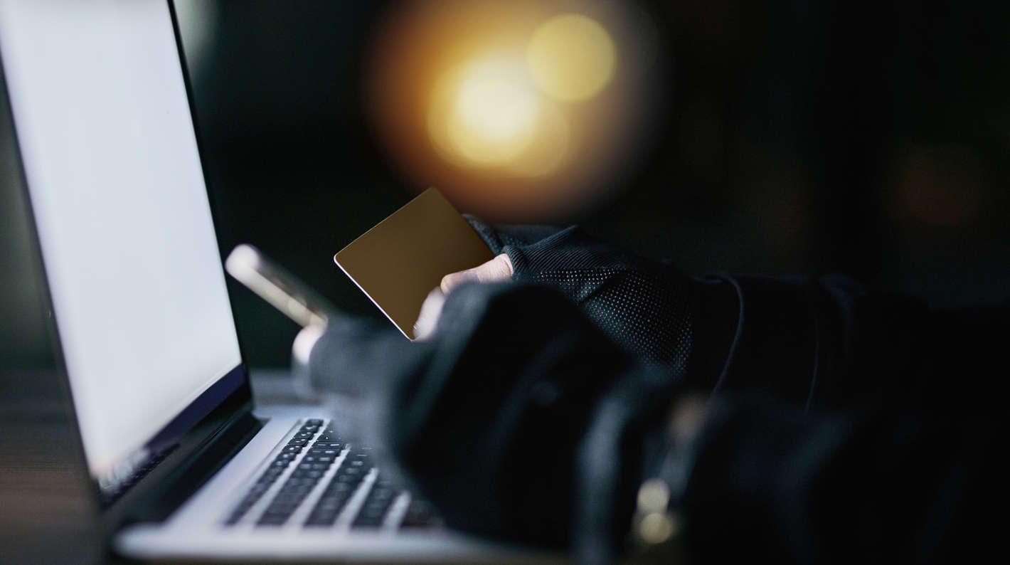 Hænder iført handsker som sidder foran en laptop med et kort og en telefon i hånden